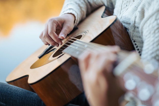 Close up of a young girl playing the guitar Young female mastering skills of playing the guitar outdoors in fall nature