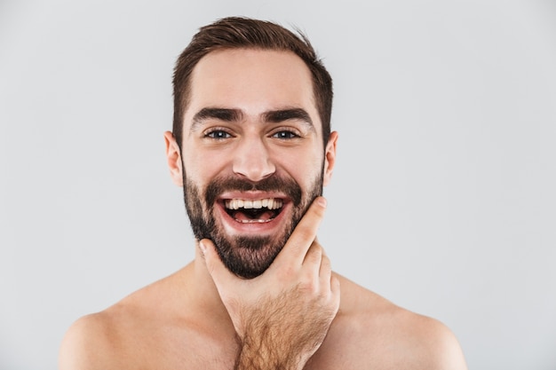 Close up of a young handsome bearded shirtless man standing isolated over white