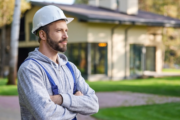 Close up of young male engineer in hard hat looking away posing with arms crossed