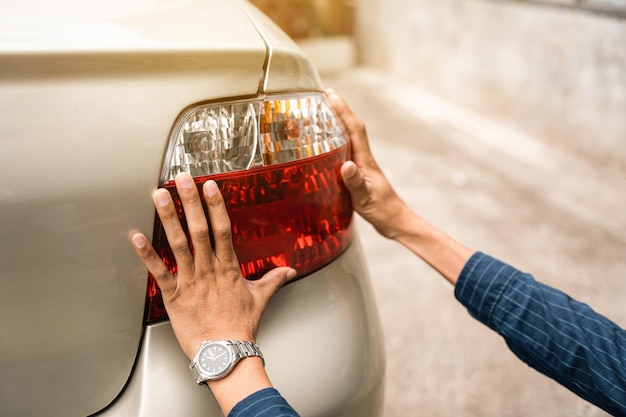 Close up young man hands auto mechanic checking tail light Automobile servicing and repair concept