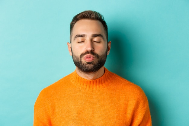 Close-up of young man in sweater pucker lips, close eyes and waiting for kiss, standing  