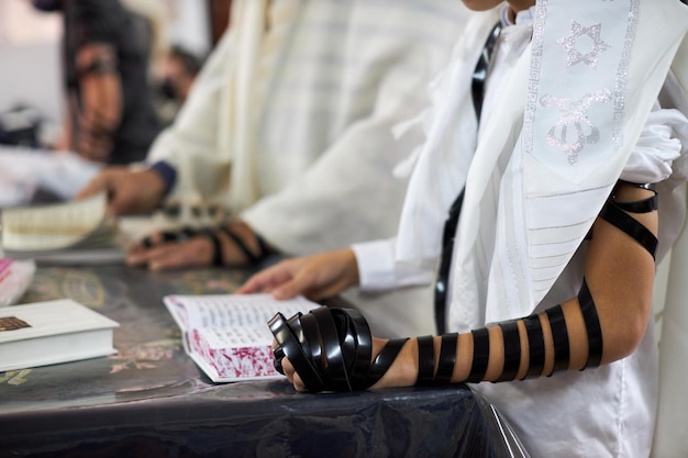 Close up young men reading jewish prayer and a hand with tefillin and talitselective focus soft focu...