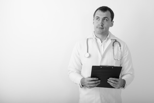 Close up of young muscular man doctor thinking while holding clipboard