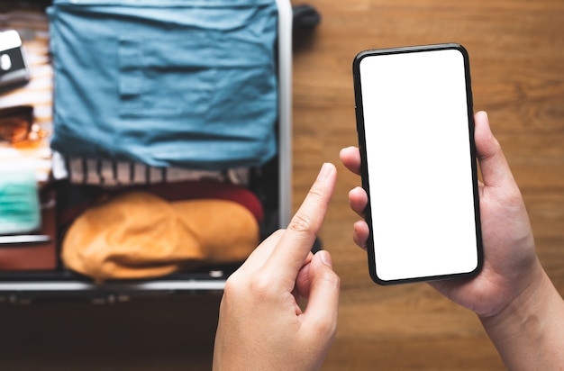 Close up young person using smartphone with blank screen on suitcase.