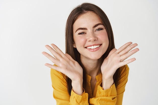 Close-up of young pretty woman showing perfect smile and face, smiling at camera, standing over white wall