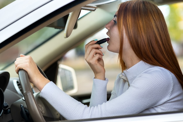 Close up of a young redhead woman driver correcting her makeup