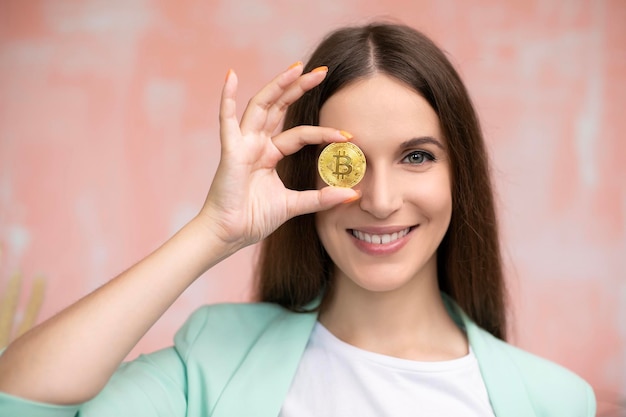 Close up young smiling female is holding bitcoin in front eye Online virtual future currency