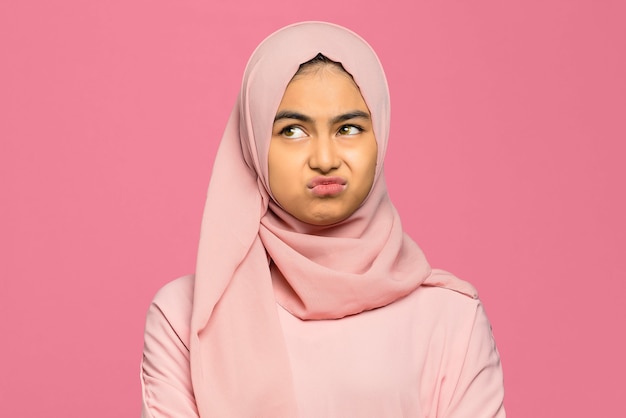 Close-up of young unhappy Asian woman on pink background