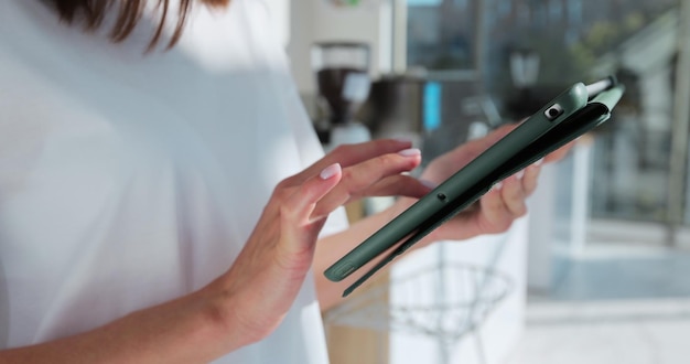 Close up of young woman barista using digital tablet at counter and taking orders from clients in cafe