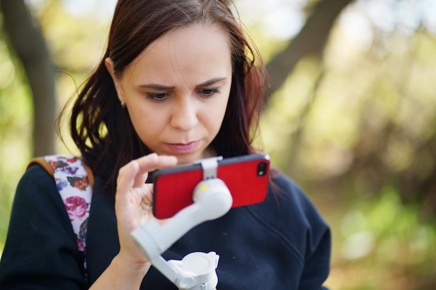 Close up of young woman browsing smartphone in countryside Portrait of female taking video on mobile phone with stabilizer outdoors