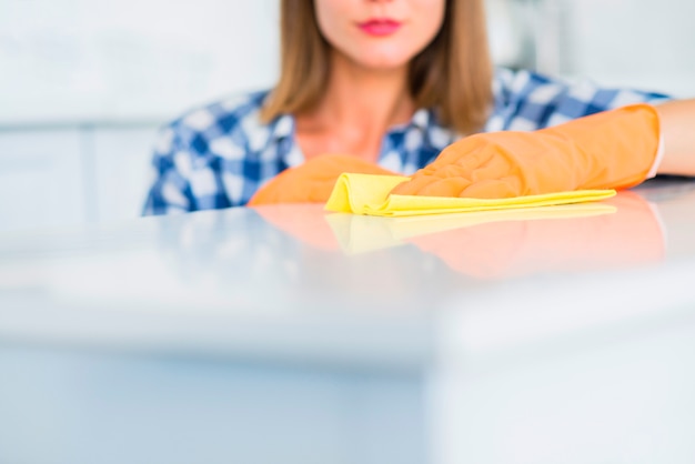 Close-up of young woman cleaning the white surface with yellow duster