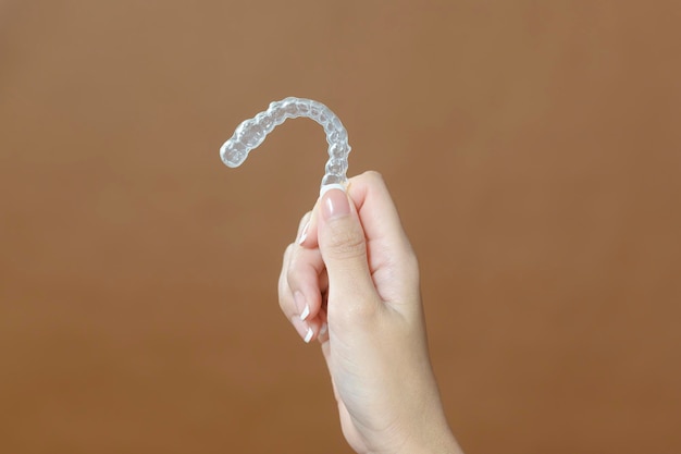 Close up young woman hand is holding Invisalign over brown background