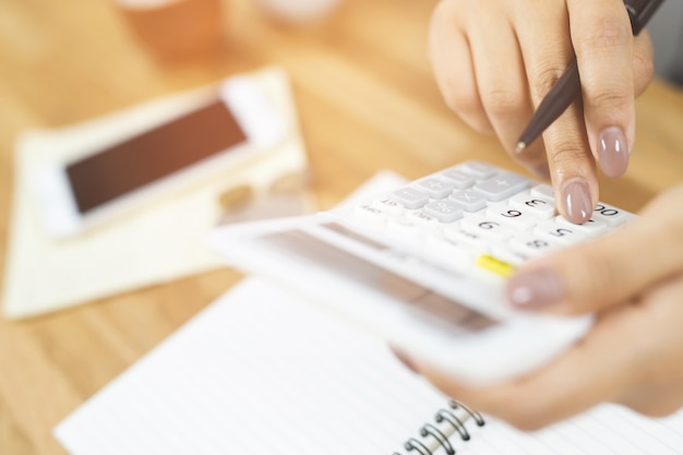 Close up young woman hand is writing in a notebook and using calculator counting making notes Accounting at doing finance at home office.