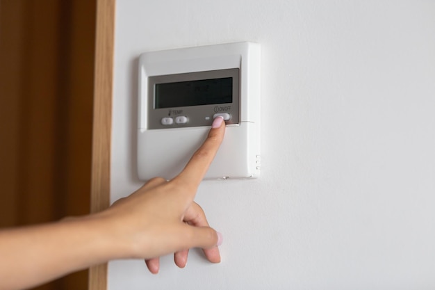 Close-up of a young woman's hand pressing the onoff button of the air conditioner or heater.