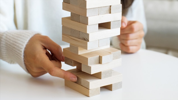 Close-up of young woman's hands is pulling out the brick from wooden tower