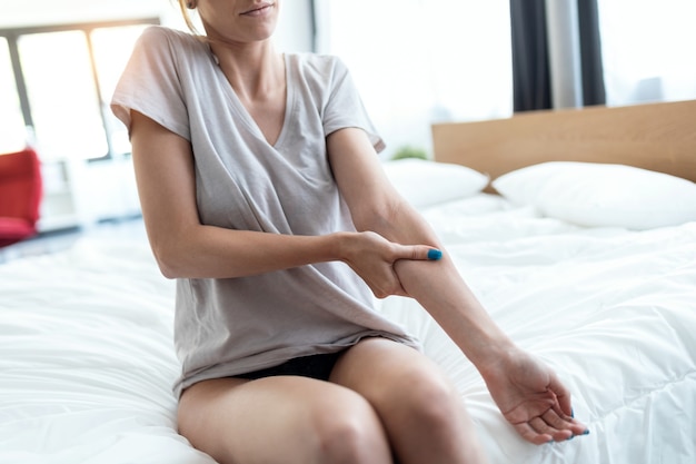 Close up of young woman sitting on the bed with muscle pain. Fibromyalgia concepts.