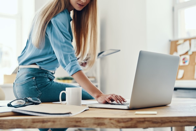 Close up of young woman in smart casual wear using laptop while working in the office