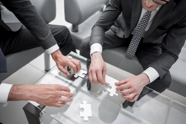 Close upbusiness partners putting together a puzzle sitting at office desk