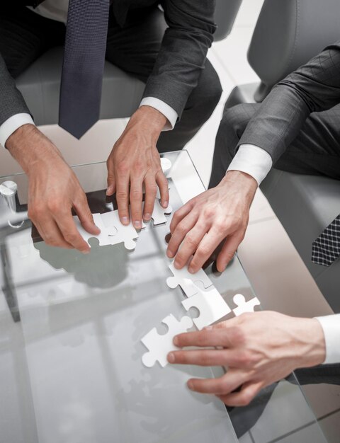 Close upbusiness people putting together a puzzle sitting behind a Deskthe concept of cooperation