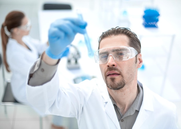 Close upsmiling scientist looks at the tube with liquid