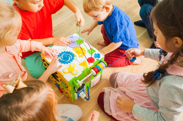 Photo close view of bright colorful plastic busy cube toy with group of kids sitting around and playing with it. educational and developing toys