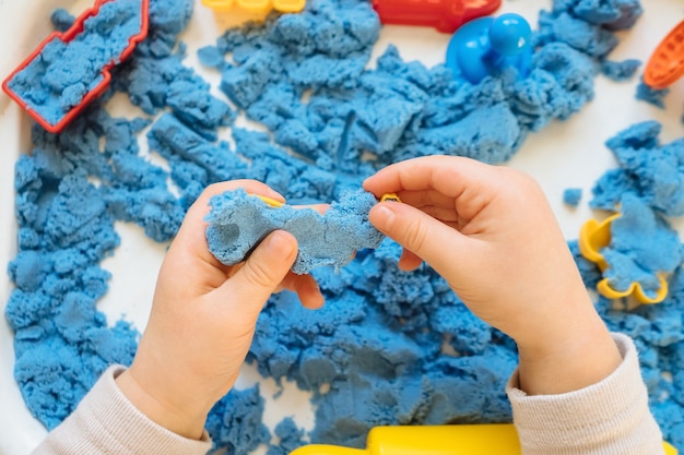 Close view of child's hands playing with kinetic sand. Children's creative game for early development and fine motor skills.