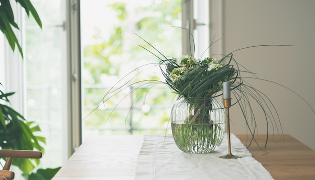 Close view of fresh flowers in glass vase standing on a wooden table in white dining room interior. Interior design in minimal style.