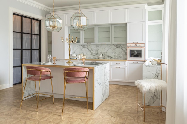 A close view of the white stylish kitchen with a cooking island in the luxurious interior of a modern apartment in light colors with stylish furniture