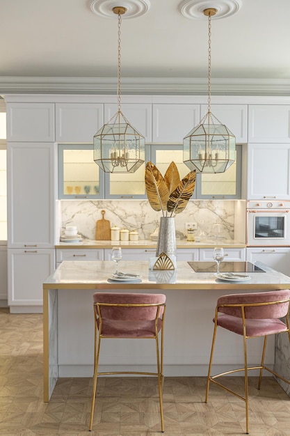 A close view of the white stylish kitchen with a cooking island in the luxurious interior of a modern apartment in light colors with stylish furniture