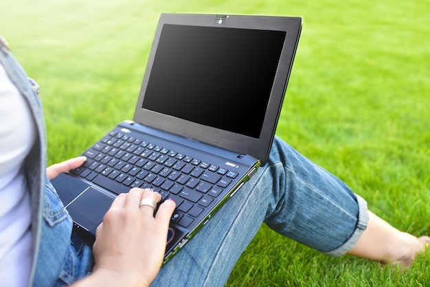 Close view of woman sitting on grass and using laptop