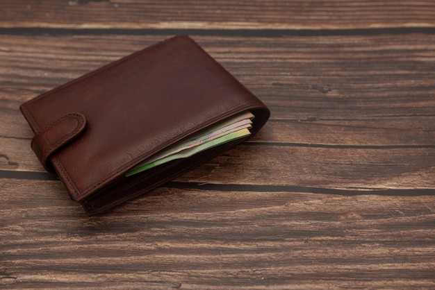 Closed men's brown wallet on a wooden brown with money.