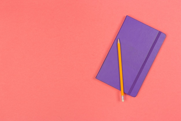 Closed note pad with pencil on colored background top view