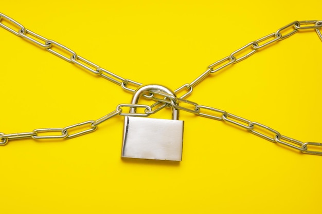 Closed padlock hanging on chains on yellow background