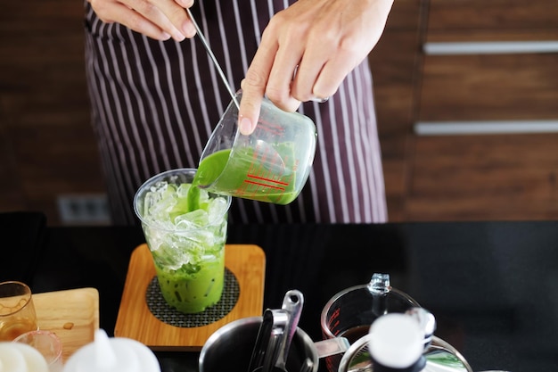 Closed up on hand of Asian barista young man pouring fresh milk is mixing with green tea in glass