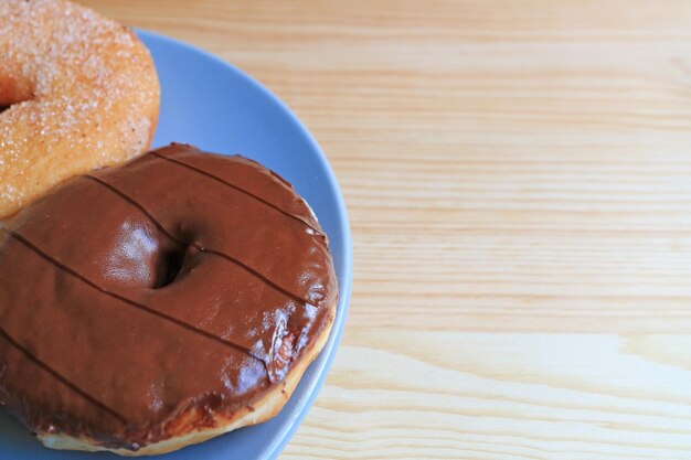 Closed up two types of doughnuts served on blue plate on the wooden table with free space