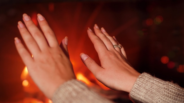 Closeup 4k foootage of young woman warming her hands at burning fire in fireplace