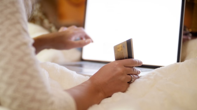 Closeup 4k footage of young woman holding credit card in hand while browsing intrnet and online stores. Concept shot of online shopping and e-commerce.