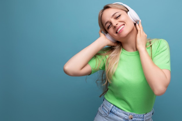 Closeup of an adorable blond girl in a casual outfit relaxing and dancing in big white headphones on