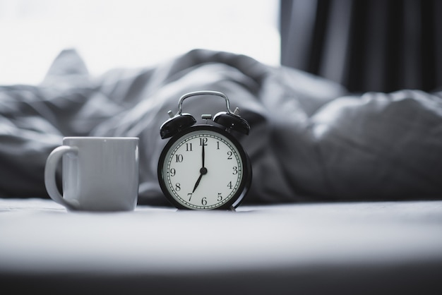 Closeup - Alarm clock have a good day with a cup of coffee on the bed in the morning sunlight, copy space.