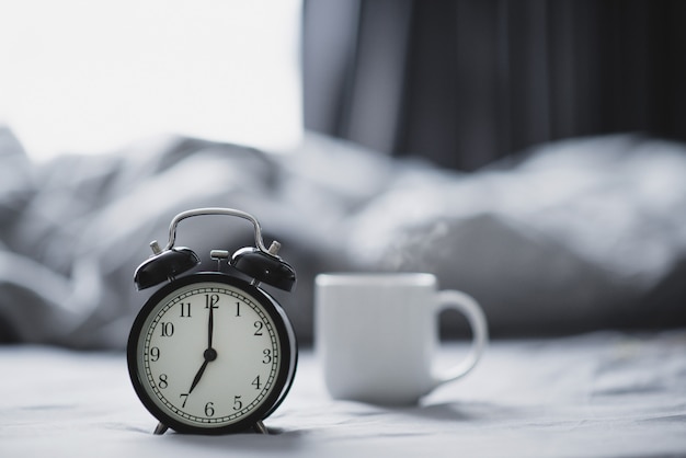 Closeup - Alarm clock have a good day with a cup of coffee on the bed in the morning sunlight.