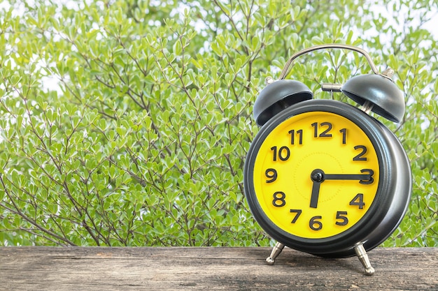 Closeup alarm clock show a quarter past six on wood desk