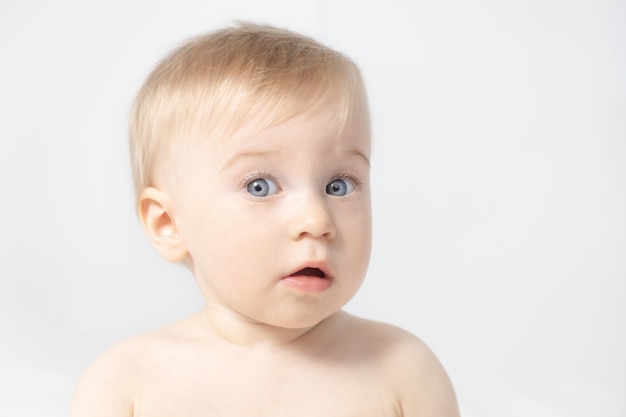 Closeup of amazed beautiful cute adorable blonde caucasian topless baby girl on grey background with open mouthlooking at cameraHealthy kid skin