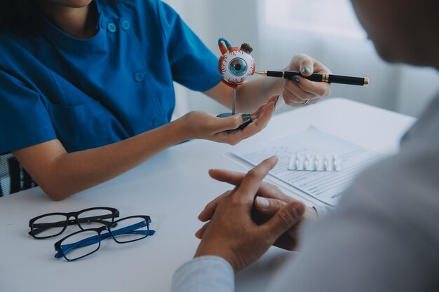 Closeup of Asian female doctor talking with elderly patient showing eyeball model and explaining eye disease in hospital