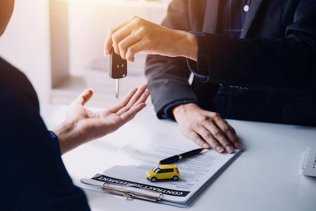 Closeup of Asian female signing car insurance document or lease paper contract or agreement Buying or selling new or used vehicle with car keys on table