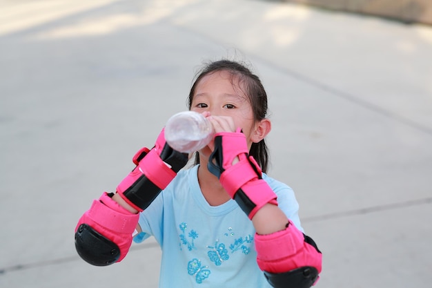 Closeup Asian little girl child wear safety and protective equipment drinking water from bottle with looking at camera