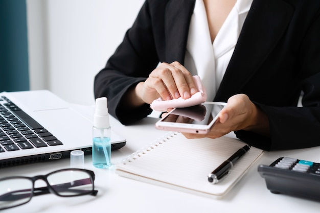 Closeup of Asian woman cleaning smartphone by alcohol spray over a work desk in office