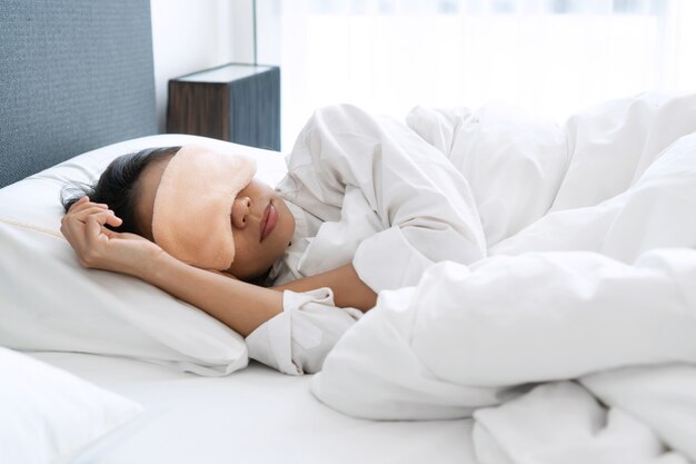 Closeup of Asian woman in sleeping mask sleep on comfortable white bed in the morning.