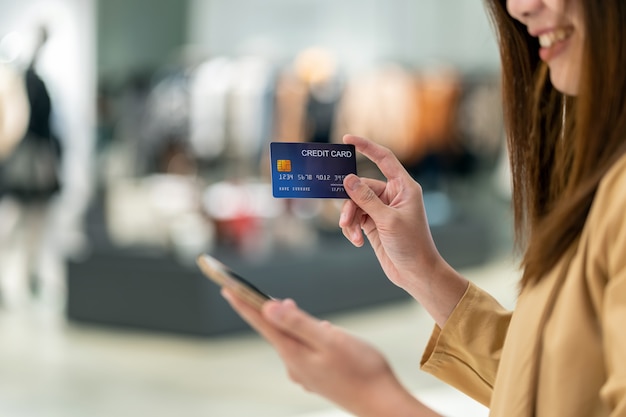 Closeup Asian woman using credit card with mobile for online shopping in department store