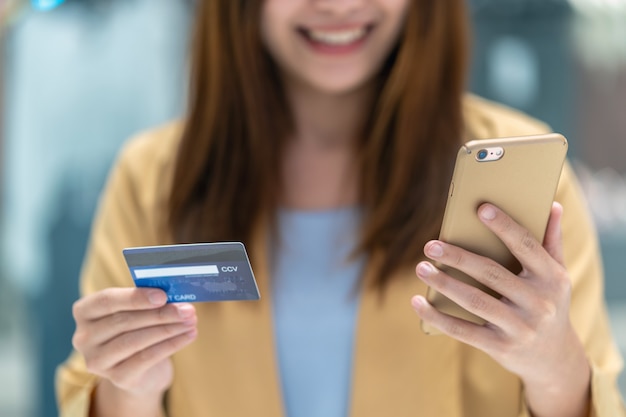 Closeup Asian woman using credit card with mobile for online shopping in department store