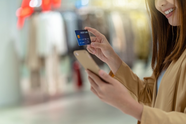 Closeup Asian woman using credit card with mobile for online shopping in department store